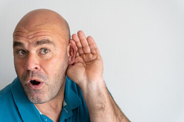Portrait of middle-aged Caucasian man with hand behind ear listening to gossip, on white background.