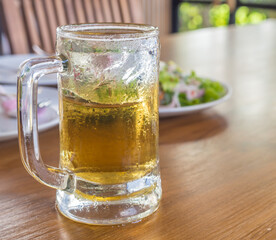 fresh beer with big round ice in a glass on a wooden table with side dish
