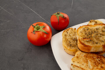 plate with crispy garlic bread with oregano on a table, decoration with fresh tomatoes, traditional and artisanal food, texture detail, background