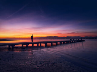 Fototapeta premium Woman from behind looking at the sunset from a pier