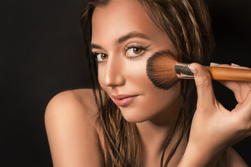 Young woman applying dry cosmetic foundation to her face