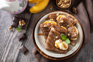 Celebrating Pancake day, healthy breakfast. Delicious homemade chocolate crepes with nuts, caramel, bananas on rustic wooden table.