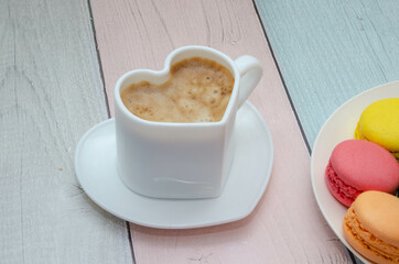 Delicious fragrant coffee in a heart-shaped mug with colorful sweet macaroons
