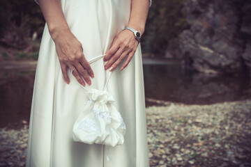 Close-up of bride holding white wedding bag. Copy space