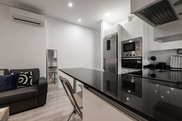 Kitchen with stainless steel appliances, white cabinets with black marble island and living room with sofa on the opposite side