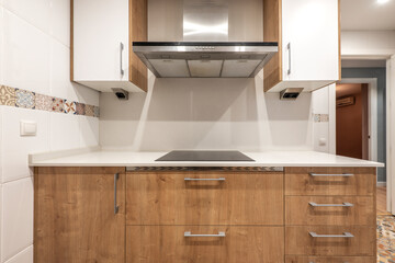 Kitchen with wooden furniture combined with white furniture and a large stainless steel hood over the ceramic hob