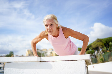 Mature woman working strength training push ups against sky with copyspace.