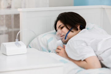 A nebulizer mask on the girl's face  laying in the bed. The concept of treatment of respiratory diseases, chronic bronchitis, recovery.