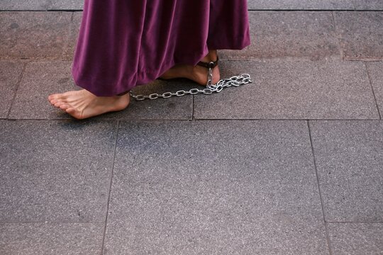 Feet of a barefoot man walking in chains through the streets of the city in a typical Andalusian procession. Religious robe is carried by a man without shoes. Pain in the feet when walking barefoot