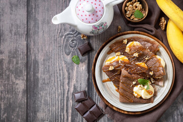 Celebrating Pancake day, healthy breakfast. Delicious homemade chocolate crepes with nuts, caramel, bananas on rustic wooden table. Top view flat lay. Copy space.