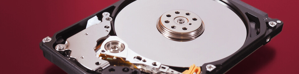 A disassembled open hard disk drive HDD of a computer or laptop lies on a red matte surface. IT&C closeup. Banner about computer hardware and equipment. Data storage headline. Macro