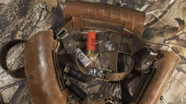 the hand is dropping shotgun cartridges near a cartridge belt on the camouflaged surface