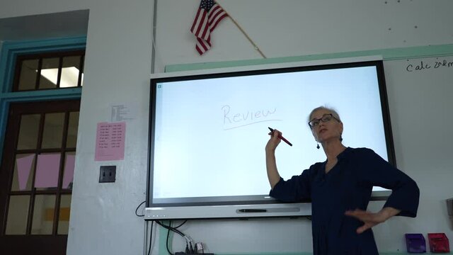 Female teacher writing on an interactive whiteboard in an empty classroom.