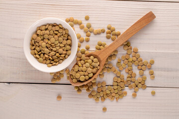 Uncooked organic green lentils with a white saucer and a wooden spoon on a wooden table, macro, top view.