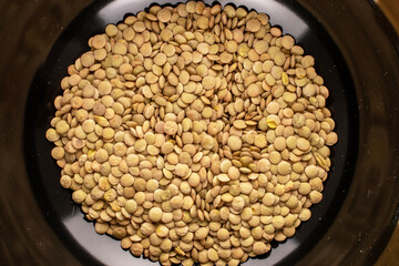 Uncooked organic green lentils in a black ceramic dish, macro, top view.