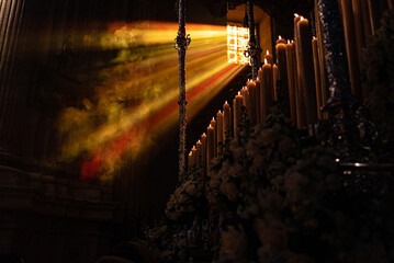 Procession during Holy Week in Sevilla, Andalucia, Spain. Incense smoke is seen in the beam of light coming in from the church window. Religious festival for Catholics - obrazy, fototapety, plakaty