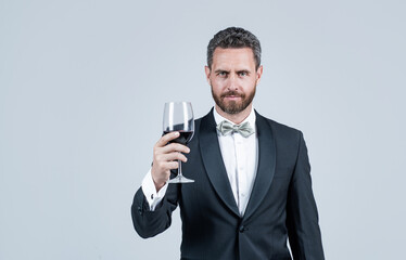 handsome tuxedo man cheers with glass of red wine hold gift box behind back, copy space, sommelier