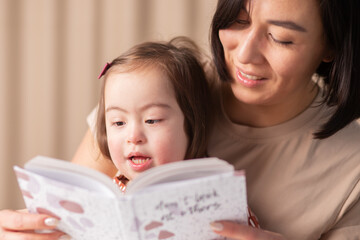 formation of the skills of a child with down syndrome, girl with her mother and a book at home read