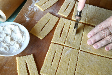 Mani donna che preparano i tradizionali dolci di carnevale italiani chiamati chiacchiere su sfondo bianco. Copia spazio. Direttamente sopra. - obrazy, fototapety, plakaty