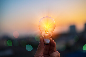 Man hands holds a house light bulb at sunset