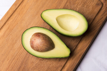 Two avocado parts on wooden desk, cut to half, seed visible