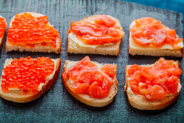 Bruschetta with trout and red caviar on a black board.