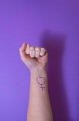 Woman's fist raised with the female symbol painted on the arm on purple background. Concept of feminism and feminist activism