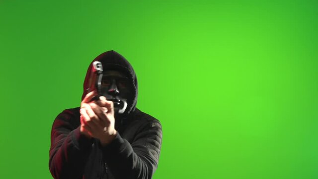 Masked man wearing a black hooded sweater carrying and pointing a gun and taunting - shot on green screen
