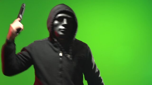 Masked man wearing a black hooded sweater carrying and pointing a gun and taunting - shot on green screen