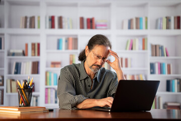 Obraz premium Angry stressed businessman reading bad news on laptop. Mad man feels frustrated about high bills, dismissal notice, bank debt, tax invoice or mistake sits at home office desk.