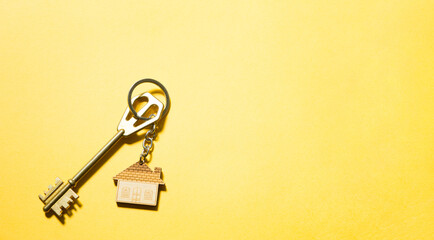 Key chain in the shape of wooden house with key on a yellow background. Building, design, project, moving to new home, mortgage, rent and purchase real estate. Copy space