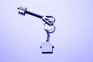 Key chain in the shape of wooden house with key on a purple background. Very peri tinting. Building, design, project, moving to new home, mortgage, rent and purchase real estate. Copy space