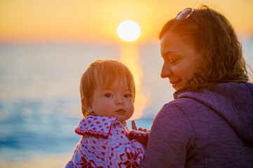 Mom and daughter admire the sunset on the shore of the winter sea. Beautiful sunset in winter....