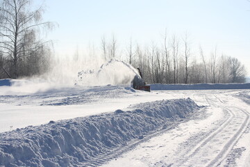 Clearing the road from snow with a snowplow on a sunny winter day
