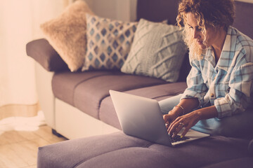 Modern lady working online with laptop computer comfortably sitting on the sofa at home. Concept of smart working lifestyle female people. Woman using notebook and relaxing