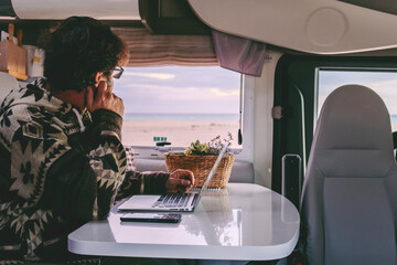 Man working inside camper van sitting at the table and looking outside the window the beautiful...