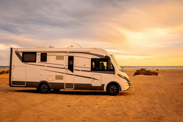 Big modern motorhome camper van parked on the ground and beautiful beach with sea and sunset lights in background. Concept of summer travel holiday vacation with camping car free