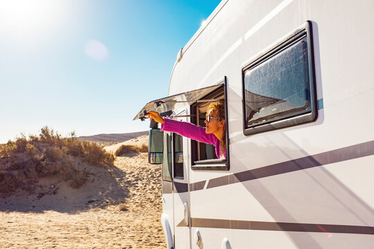 Adult tourist woman opening camper van window to enjoy the sun and freedom. Concept of travel people for summer holiday vacation inside camping car motorhome vehicle. Freedom nomad lifestyle