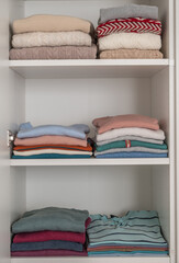 Pastel clothes folded on shelves in wardrobe