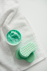 Scrub and two sea-green soaps lie on a white towel, flat lay