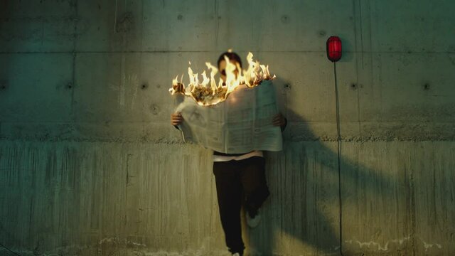 Footage of male artist with sunglasses standing near wall , holding and reading newspaper during it burns . Concept or symbol of fake or forbidden news   . Man reads burning magazine . Slow motion