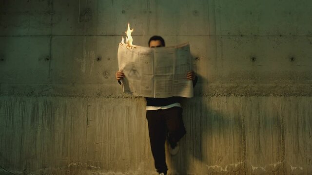 Footage of male artist with sunglasses standing near wall , holding and reading newspaper during it burns . Concept or symbol of fake or forbidden news   . Man reads burning magazine . Slow motion