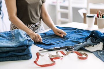 Fototapeta na wymiar Circular economy. Sustainable fashion. Reuse, repair, upcycle. Denim upcycling ideas, repair and using old jeans. Woman seamstress repair old denim jeans in Sewing studio.