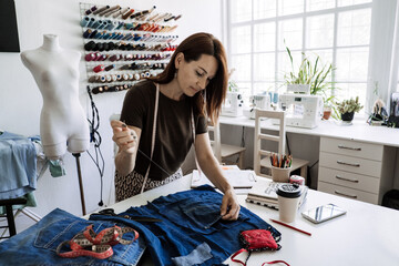 Circular economy. Sustainable fashion. Reuse, repair, upcycle. Denim upcycling ideas, repair and using old jeans. Woman seamstress repair old denim jeans in Sewing studio.