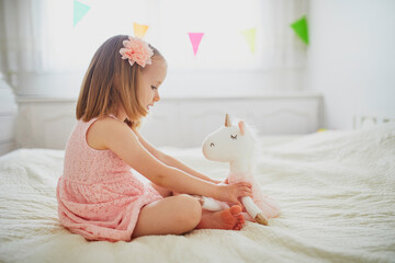 Adorable little girl in pink dress playing with unicorn