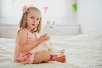 Adorable little girl in pink dress playing with unicorn