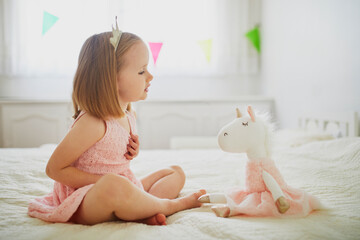 Adorable little girl dressed as princess playing with unicorn