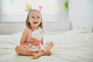 Adorable little girl dressed as princess playing with unicorn