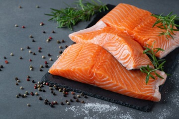 Raw salmon fillet and ingredients for cooking, seasonings and herbs on a grey background.
