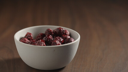 freeze-dried cranberries in white bowl on wood table with copy space